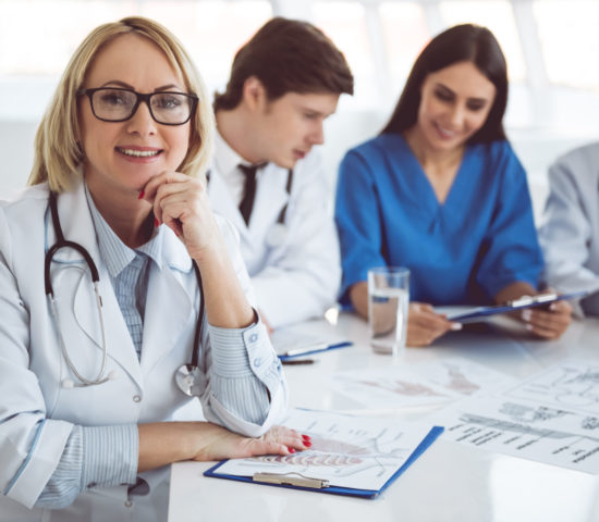Medical doctors at the conference Successful medical doctors are sitting at the conference. Beautiful mature female doctor is looking at camera and smiling